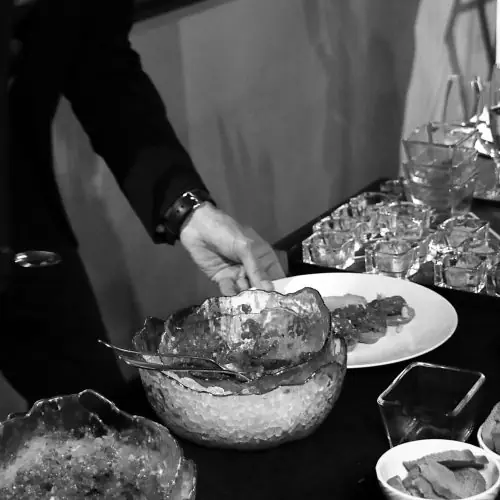 A hand arranging sliced meat on a plate beside small dishes of sauces at a buffet-style setup