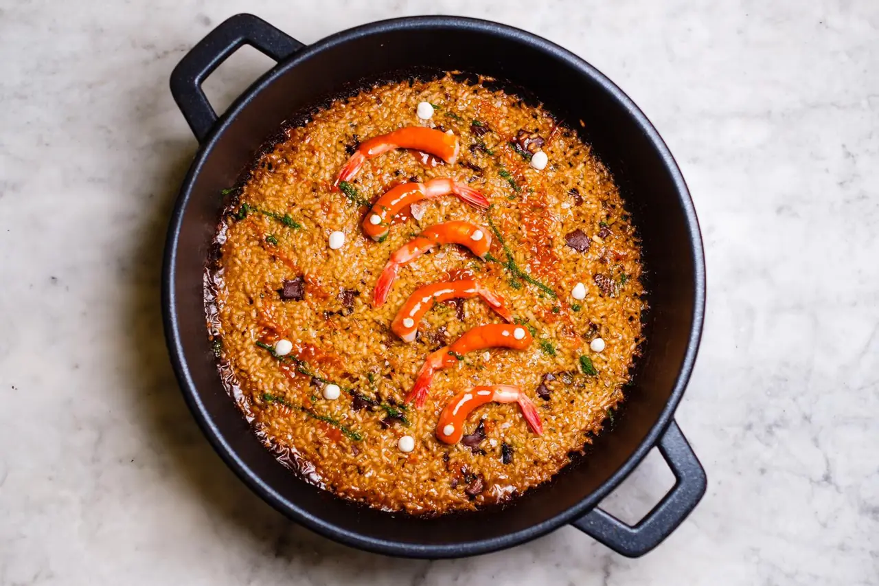 Seafood paella with grilled prawns arranged over saffron rice in a black pan, at Fonda Pepa