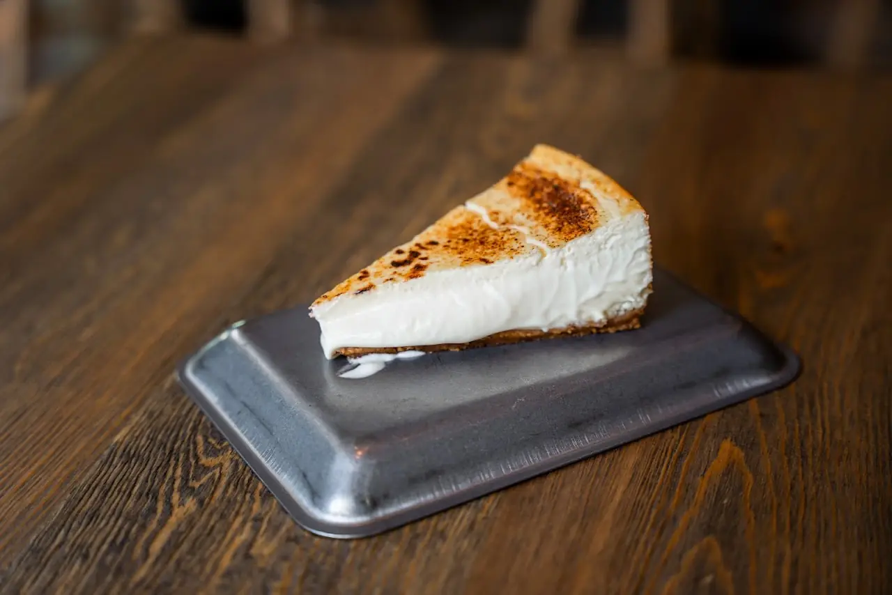 A slice of cheesecake with a torched top on a small metal tray.