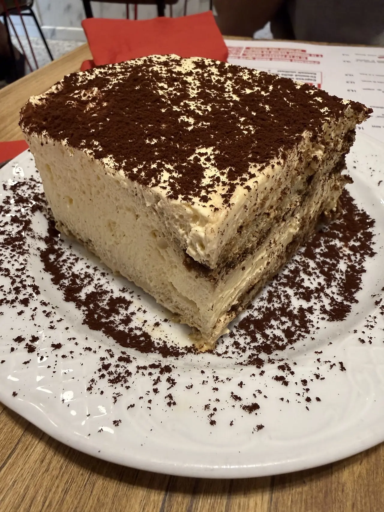 Large tiramisu slice dusted with cocoa powder, plated