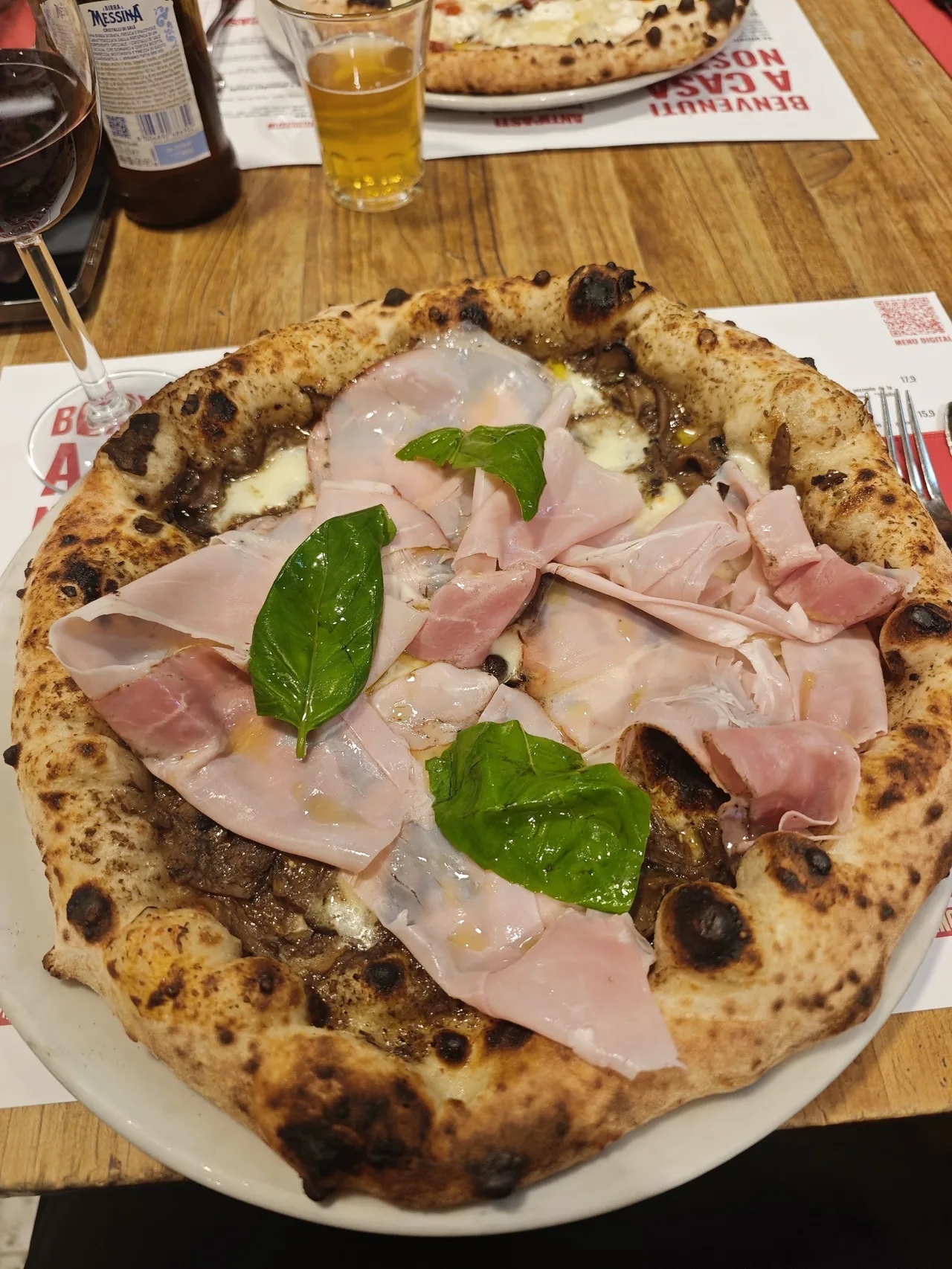 A pizza topped with slices of ham and basil leaves on a plate