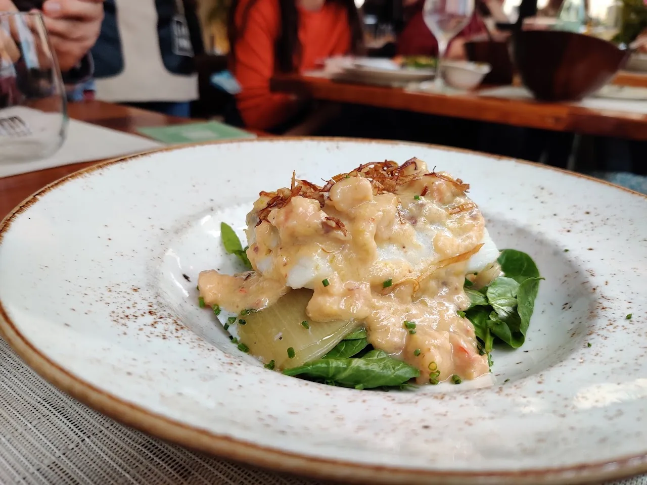 A plated dish of white fish gratin with greens on a round plate