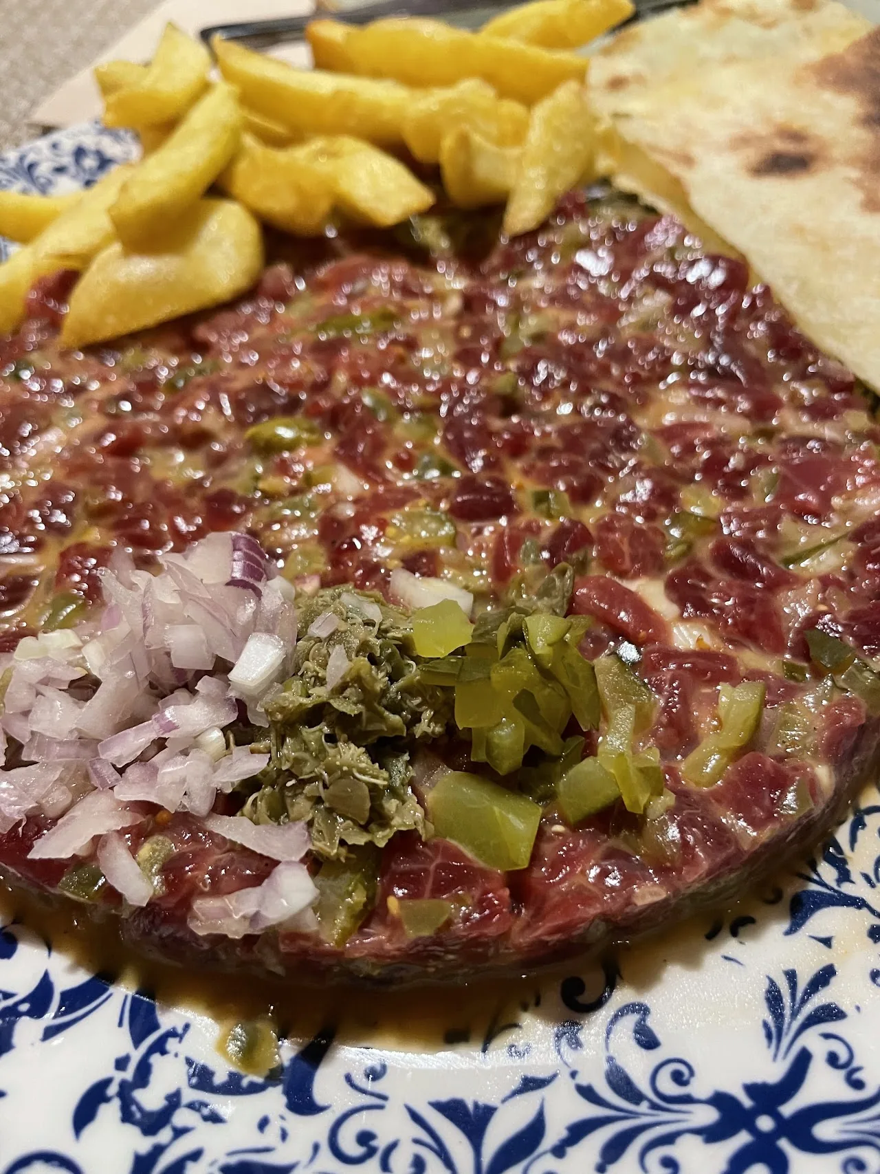A plate of raw beef tartare topped with chopped onion and pickles