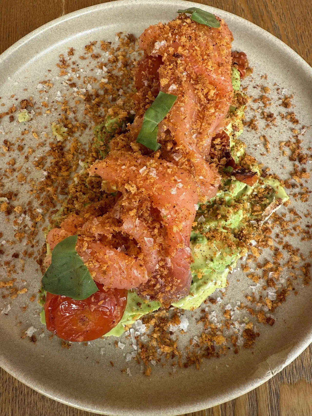 Avocado toast piled with cured salmon, crunchy crumbs and basil on a speckled plate