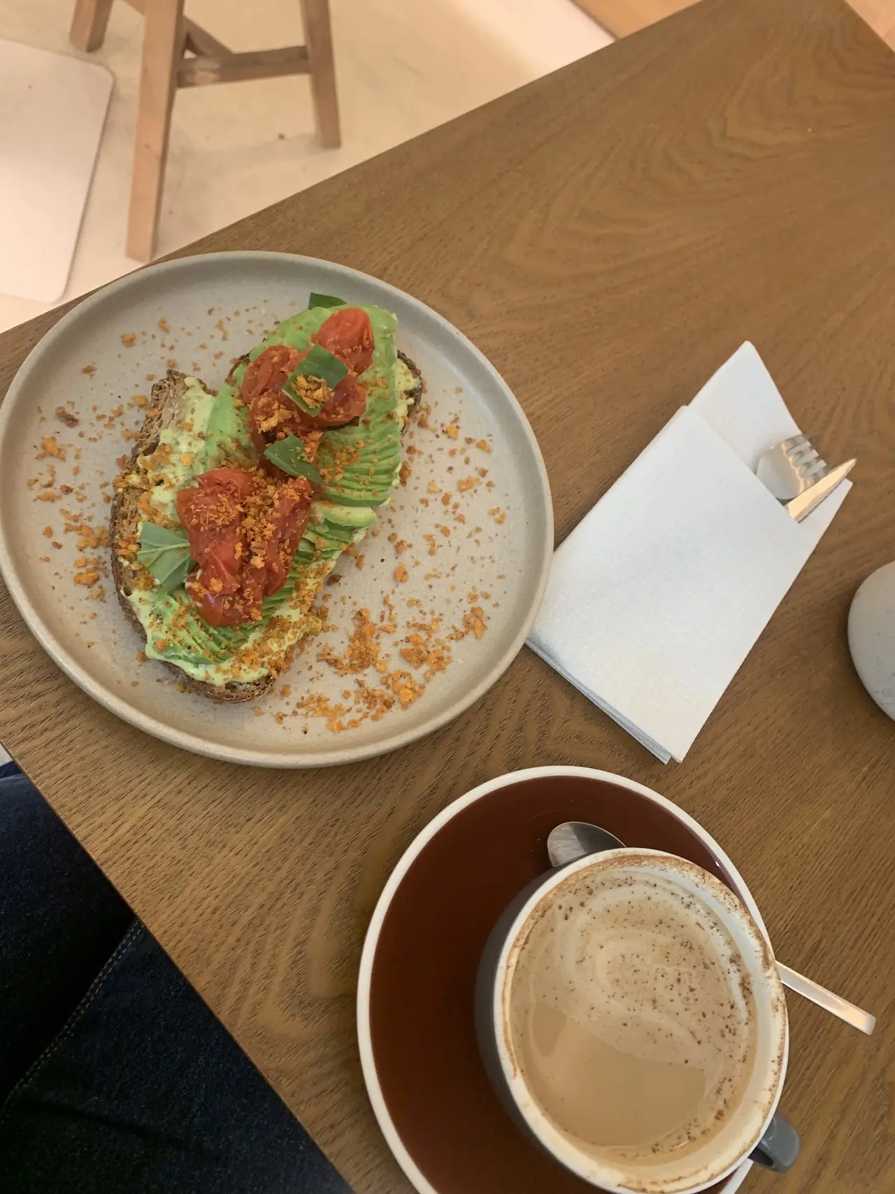 Avocado toast with tomatoes and crumbs on a grey plate, with a milky coffee and napkin
