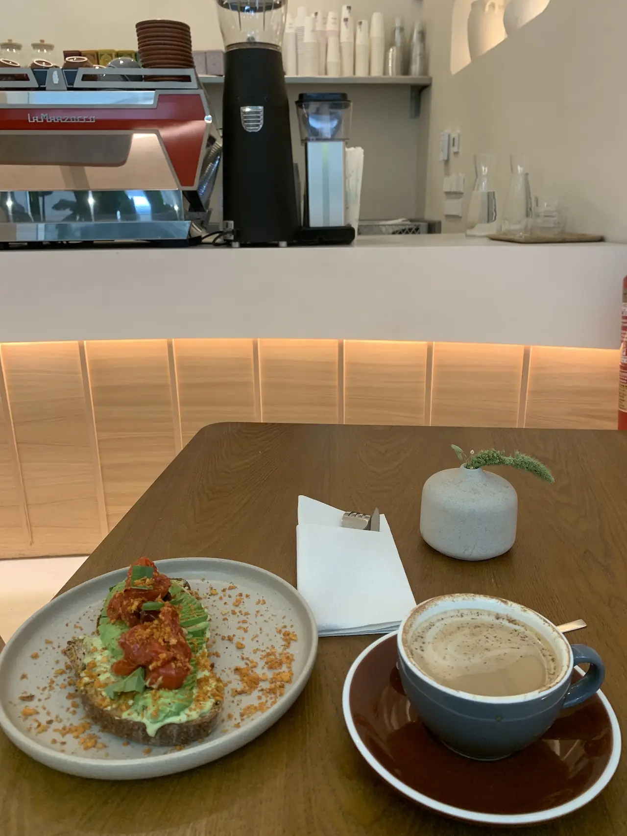 Avocado toast and a café con leche on a wooden table in front of the espresso bar