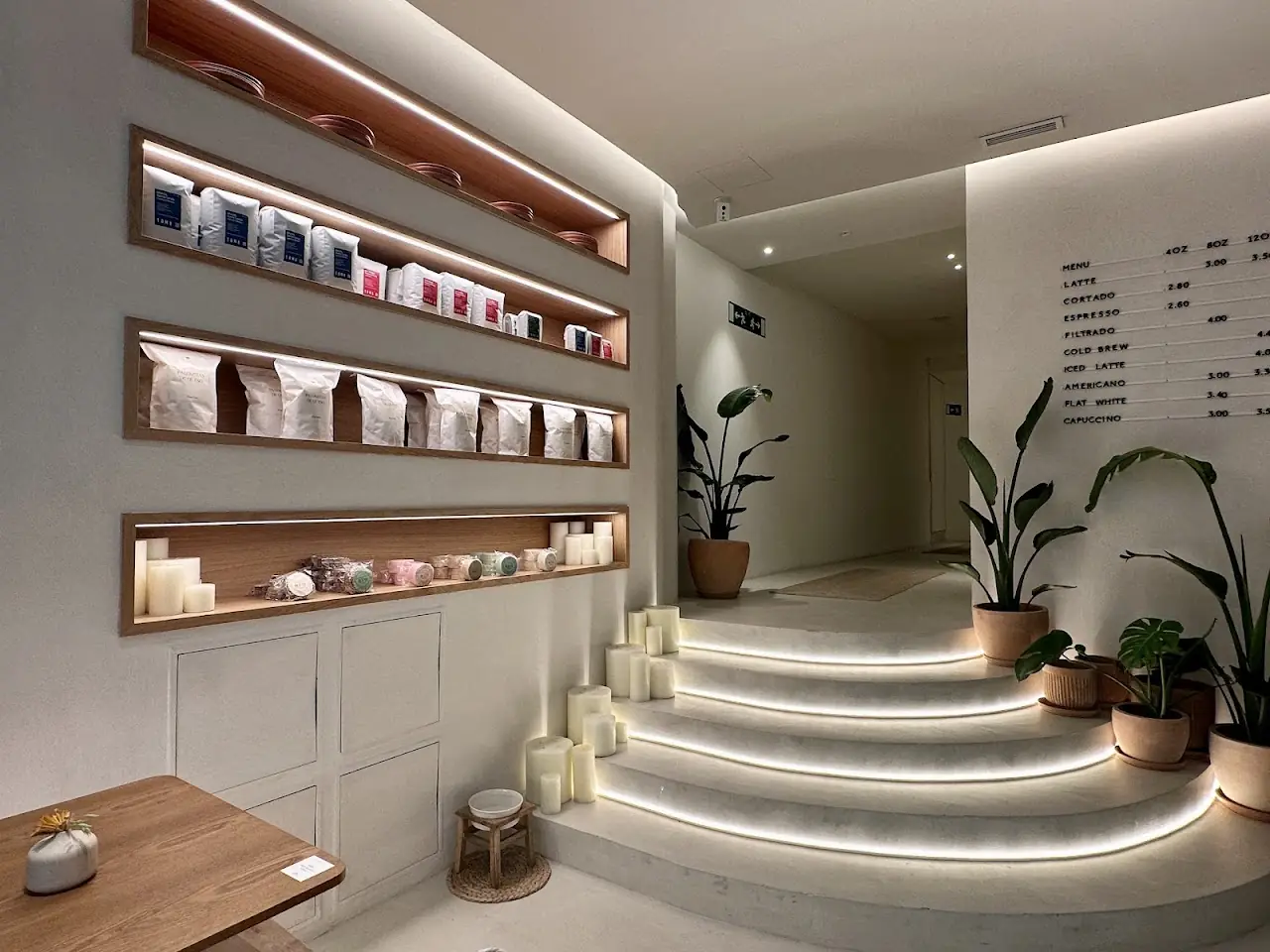 The café's white interior with backlit shelves of coffee bags and a lit staircase lined with plants