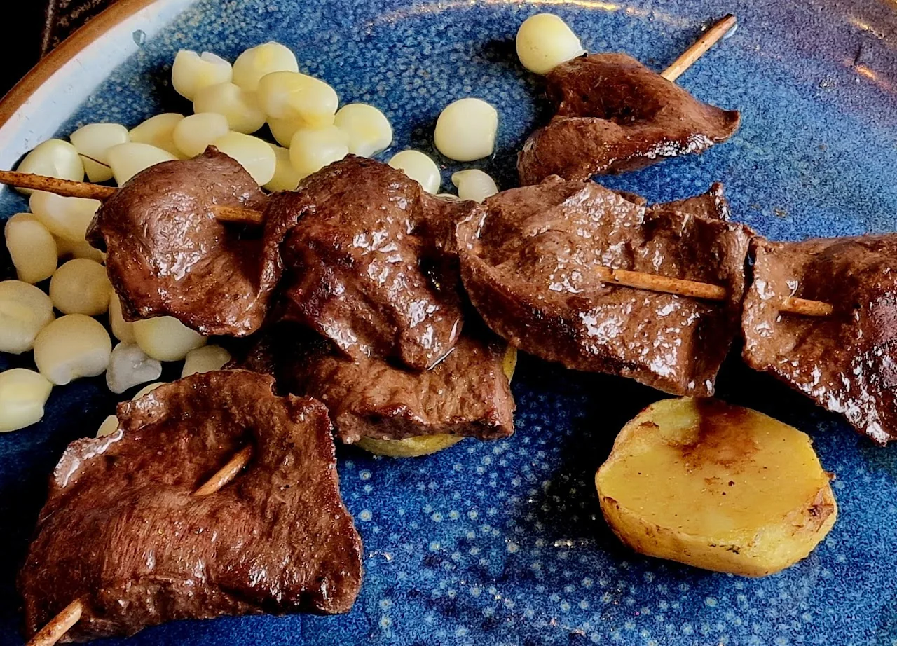 Skewered beef anticuchos with roasted potatoes on a blue plate