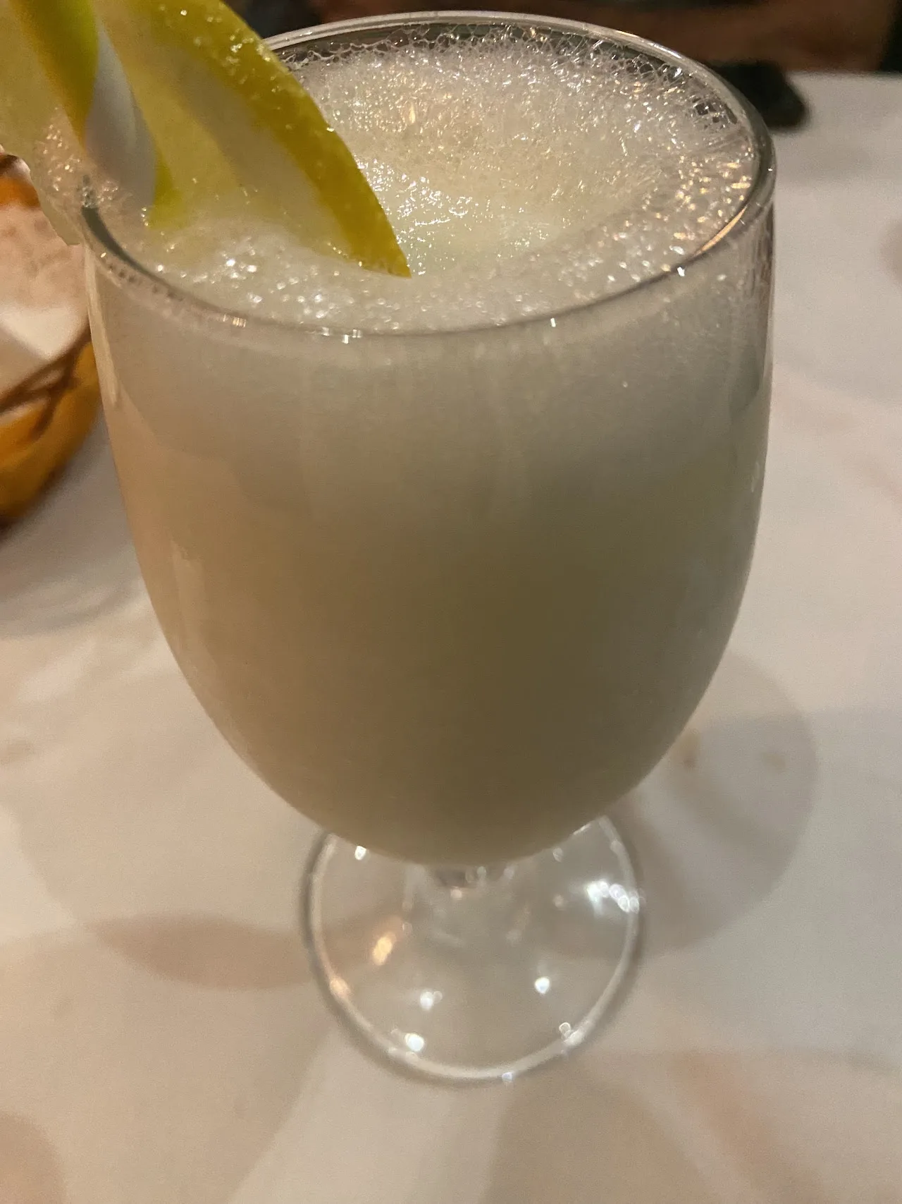 A pale yellow cocktail garnished with a lemon wedge