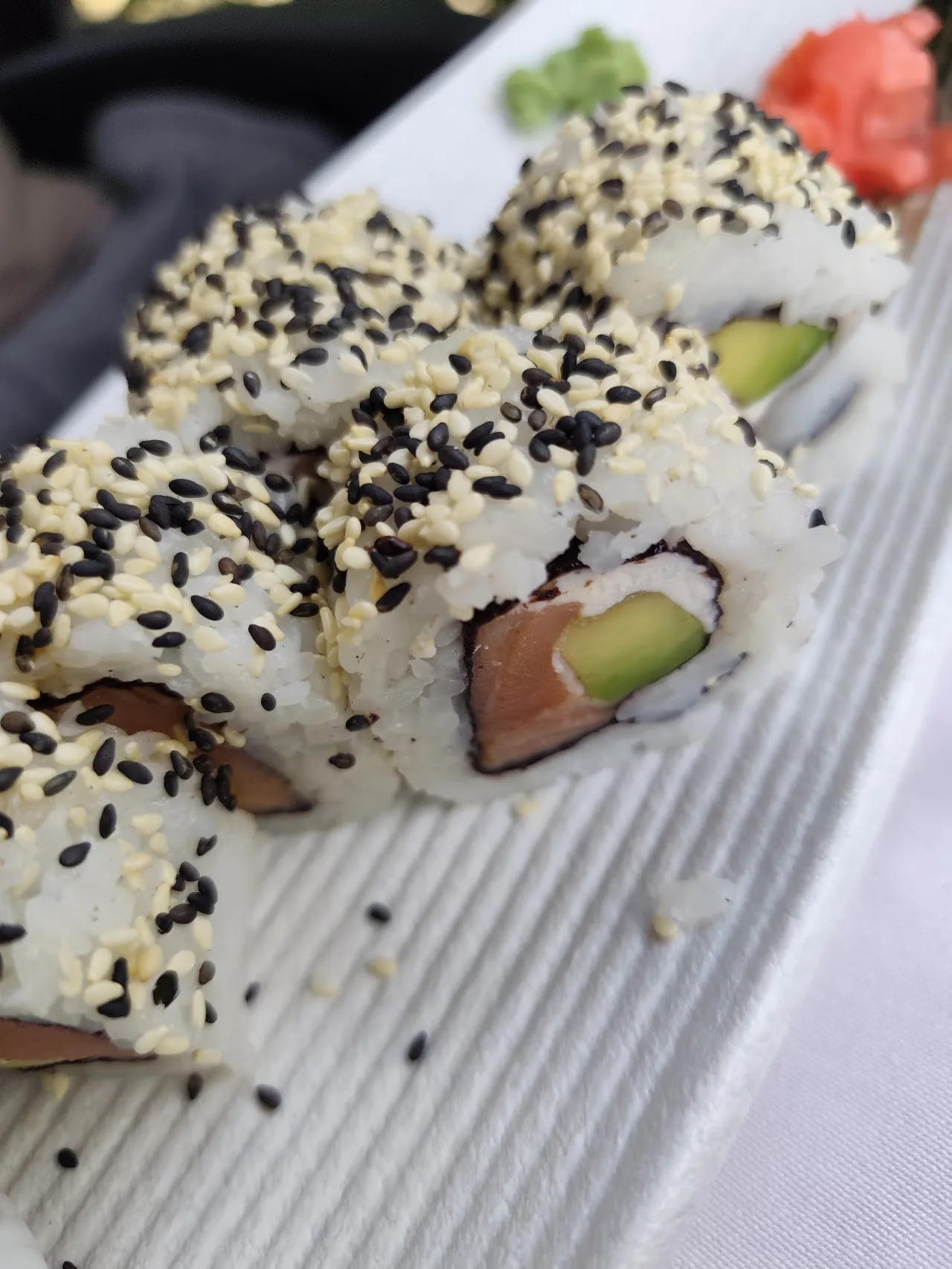 A sushi roll topped with black and white sesame seeds and avocado