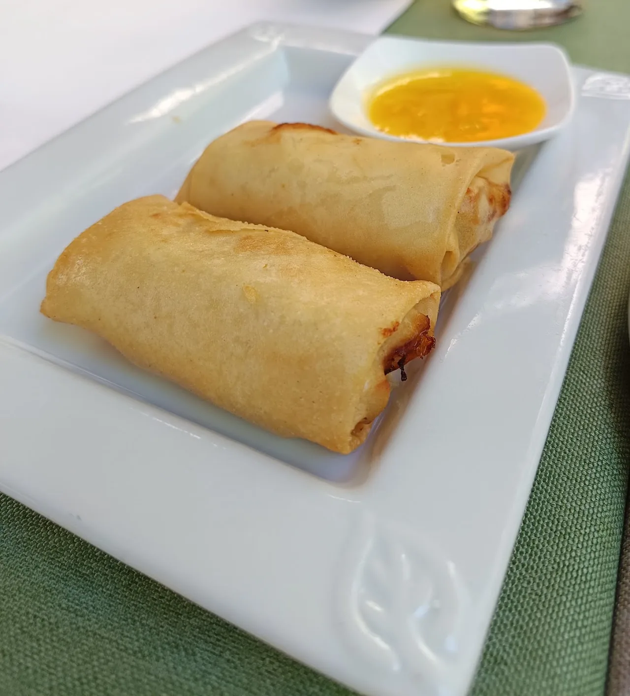Two crispy fried spring rolls on a plate with an orange dipping sauce