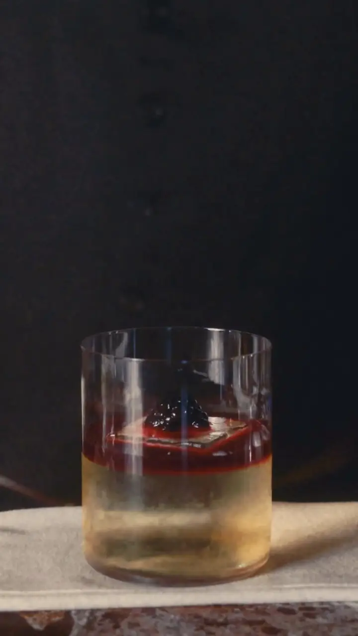 A short cocktail with a red layer and dark berry garnish in a rocks glass.