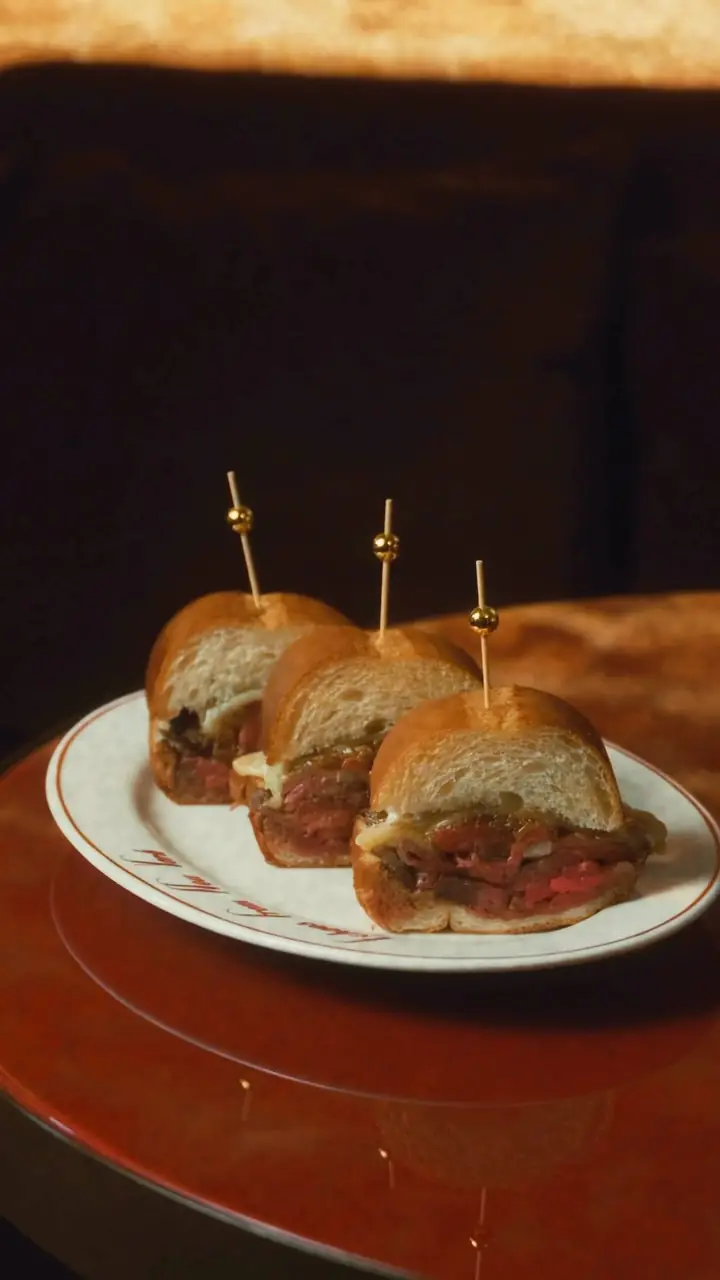 Three small steak sandwiches with toothpicks, plated on a white dish.