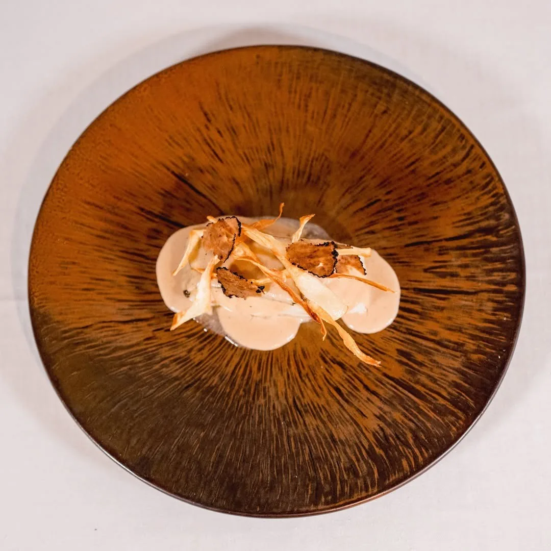 A round copper-brown plate with a pale sauce and thin fried shavings on top