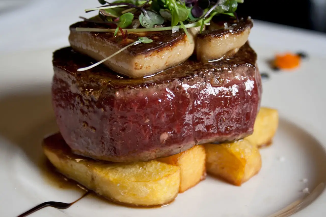 A thick seared steak topped with two seared rounds, set on toasted bread