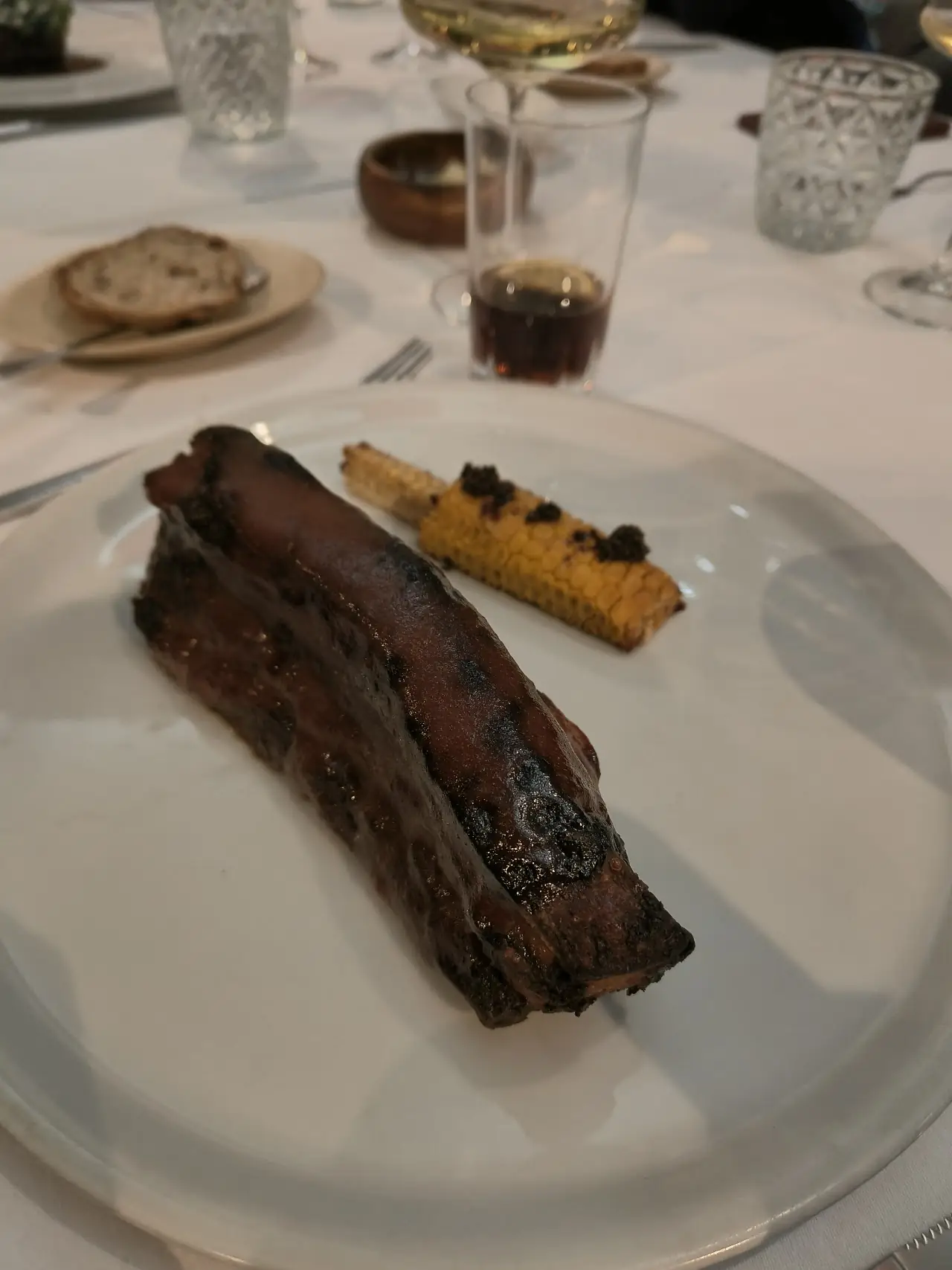 A grilled rib of meat plated with a thin bread crisp and dots of sauce.