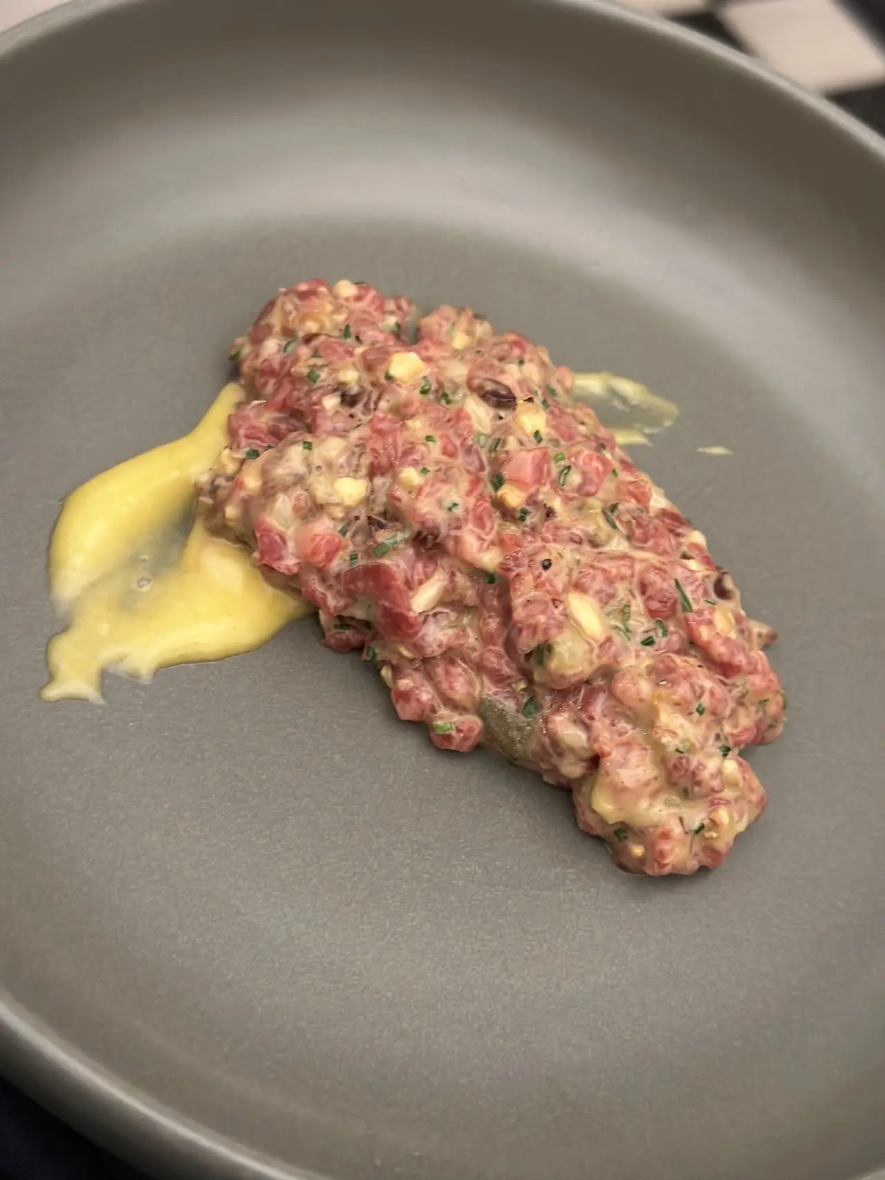 Steak tartare mounded on a plate with a swipe of egg yolk sauce