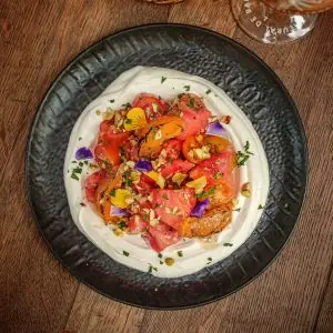 Sliced tomatoes and apricots over labneh with chopped nuts on a dark plate, Garage Bar