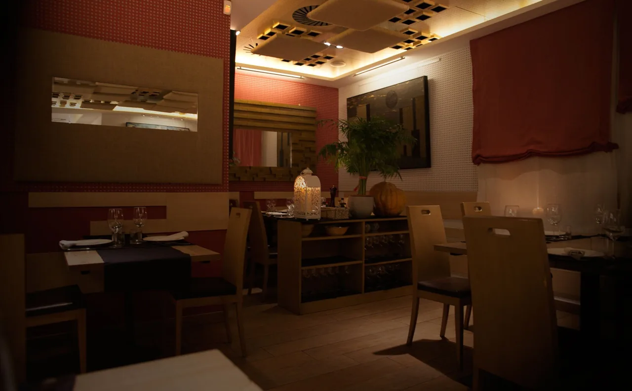 A softly lit dining room with wooden tables, chairs and a large painting