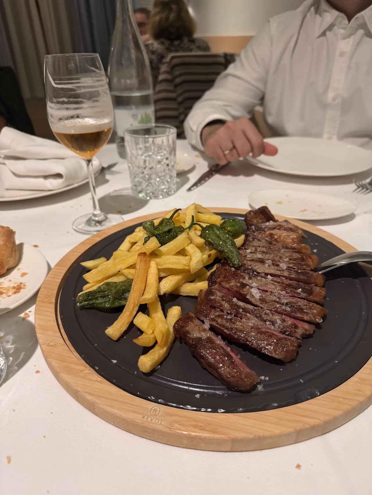 Sliced steak with fries and fried green peppers on a black platter