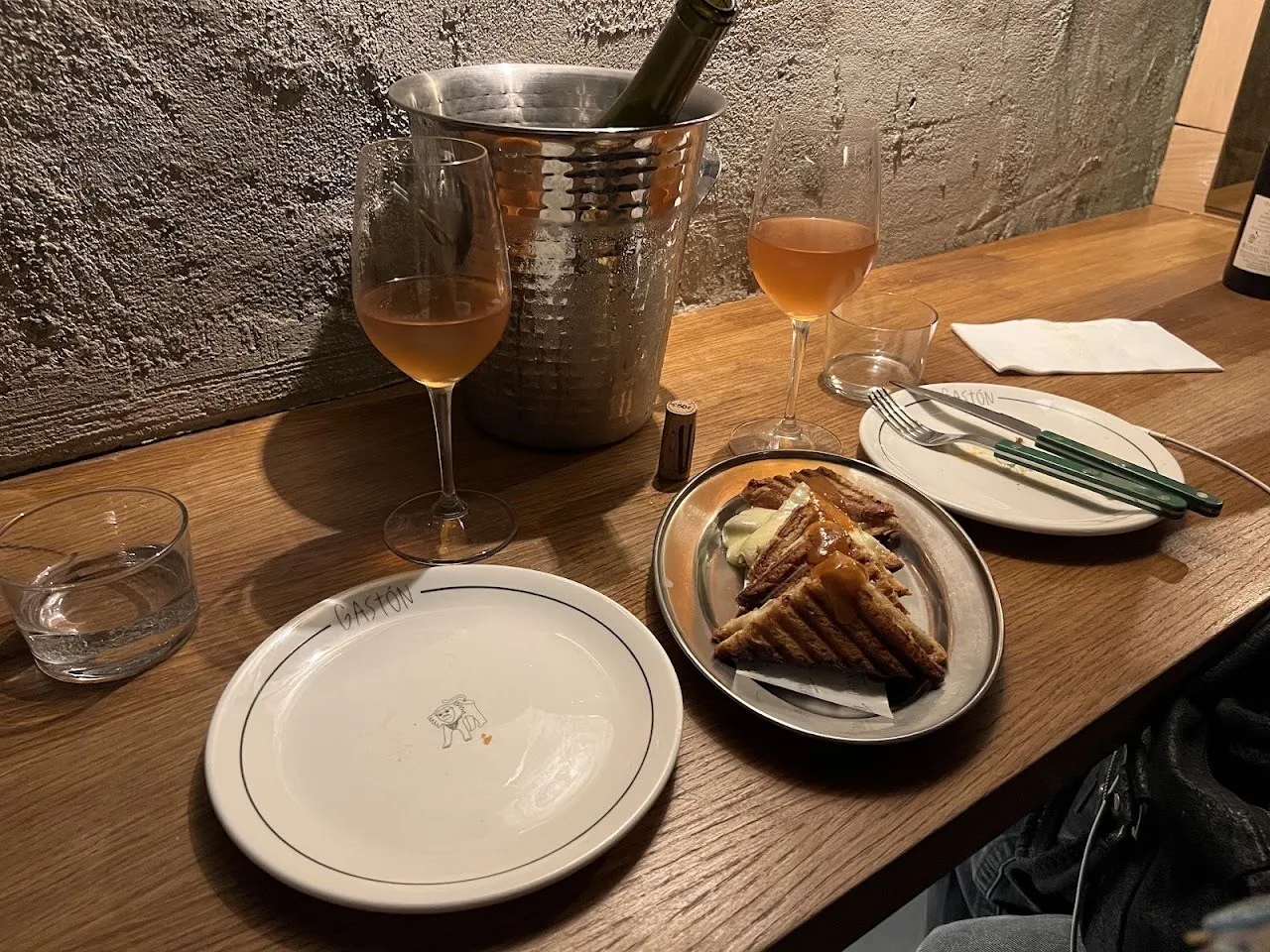 A wooden table with a glass of rose wine, an ice bucket and small plates