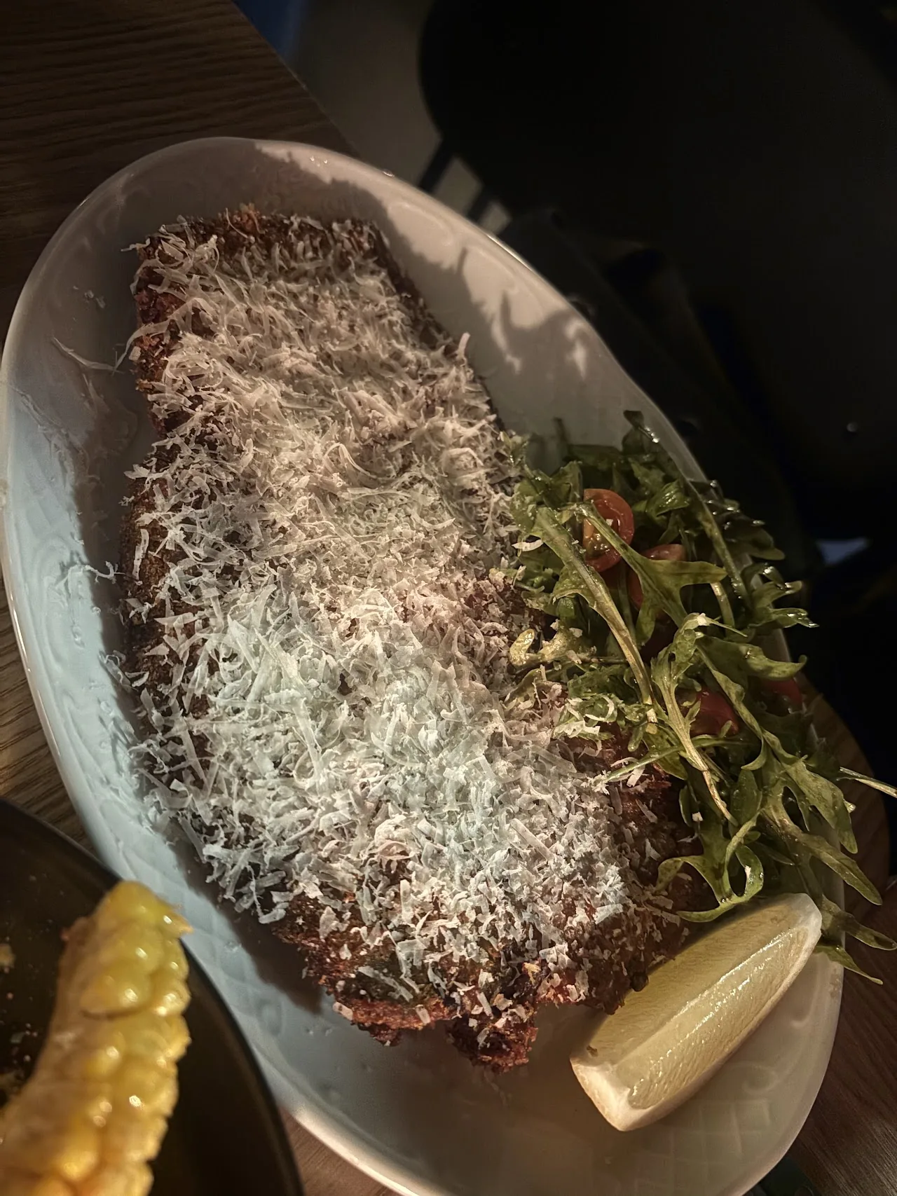 A steak topped with shaved parmesan and arugula, served with grilled corn
