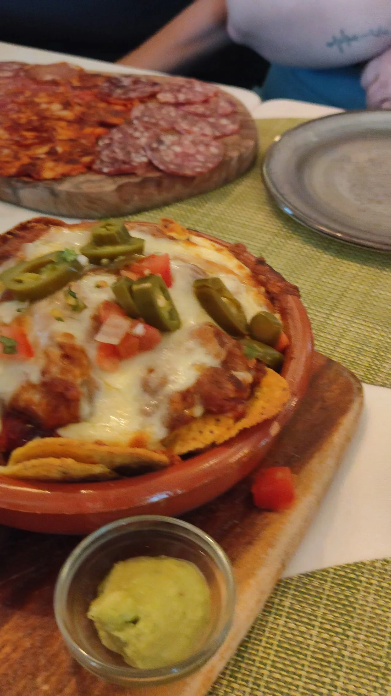 A wood-fired pizza topped with cured meat, melted cheese, and jalapeno slices