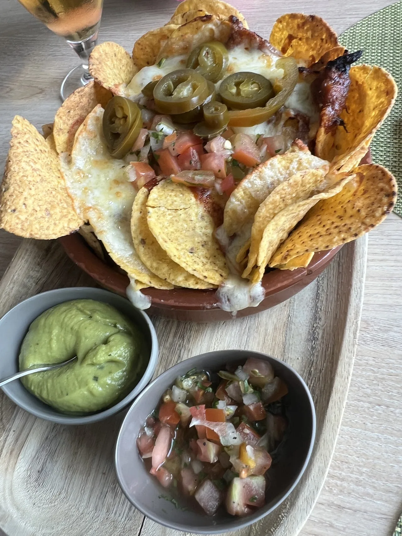 A plate of nachos with melted cheese, jalapenos, guacamole, and salsa