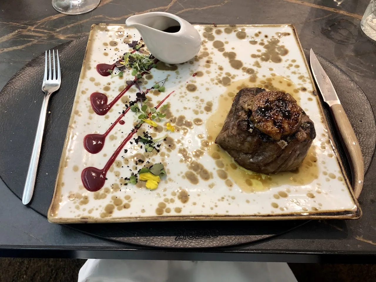 A seared piece of meat with a sauce drizzle on a square plate