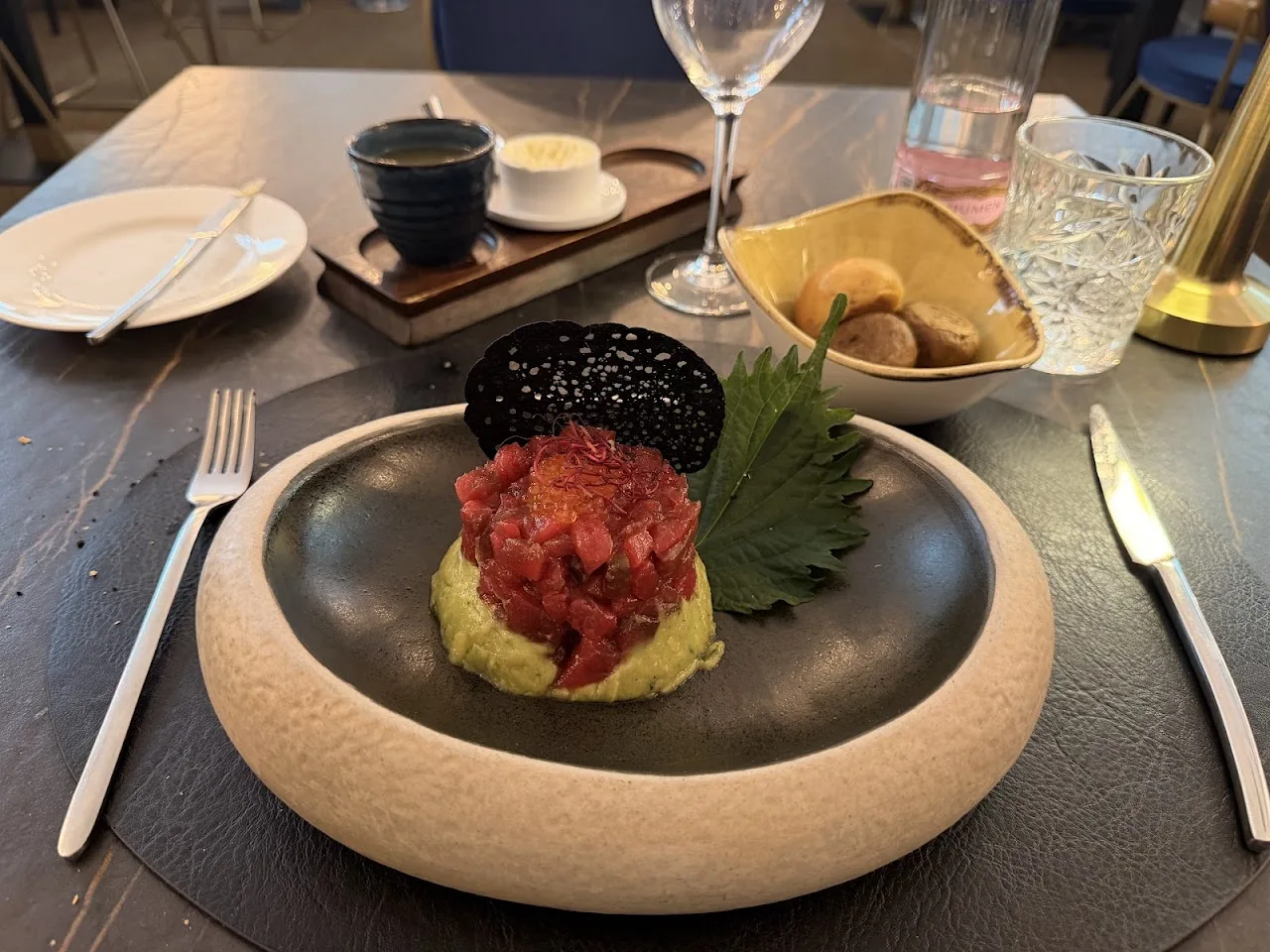 A dark bowl with tuna tartare topped with caviar, served with cocktails