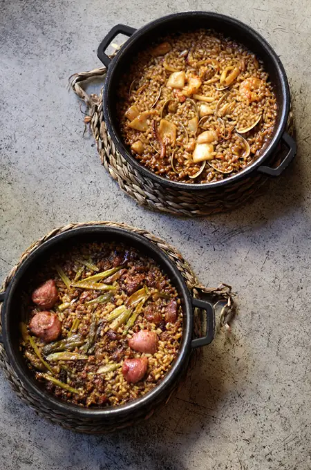 Two individual cazuelas of paella-style rice with shrimp, squid, and clams at Gats