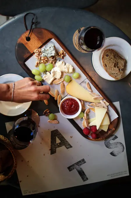 A wooden board of cheeses, walnuts, grapes, raspberries, and tomato jam with bread at Gats