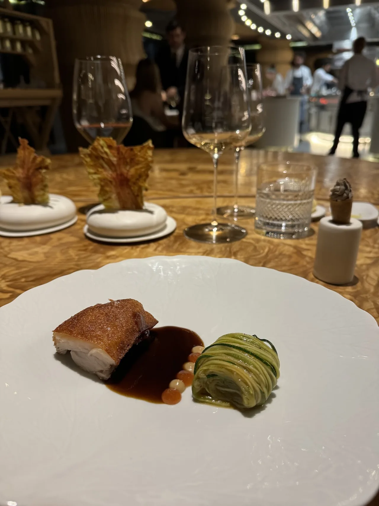 A piece of roast pork with golden crackling beside dark sauce and a rolled green vegetable on a white plate
