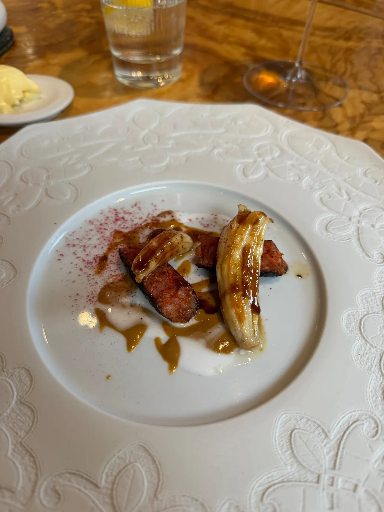 A white embossed plate with sliced meat and glazed fruit on a wooden table