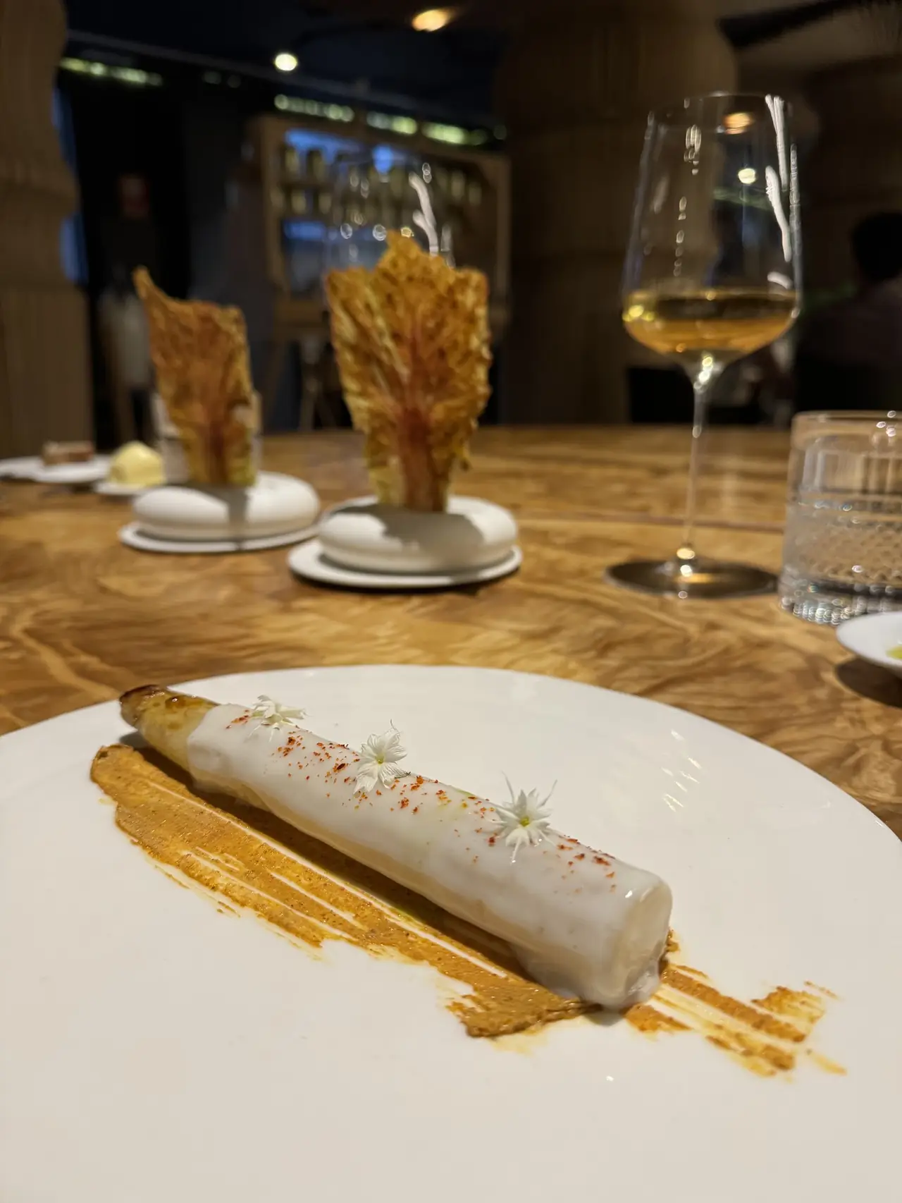 White asparagus with cream sauce, paprika dust and edible flowers over a smoked-paprika swirl on a white plate