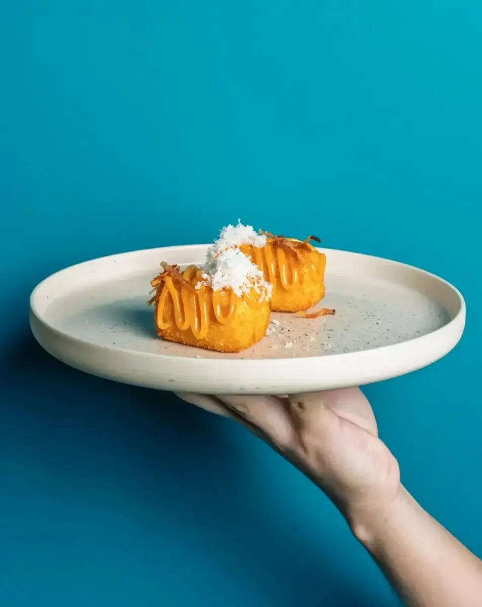 Two fried croquette-style bites with caramel drizzle and shredded coconut on a plate