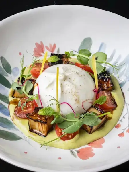 Burrata with grilled eggplant, tomatoes and herbs on a painted floral plate