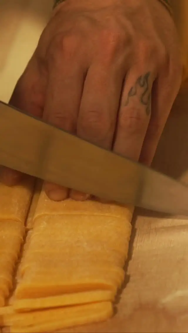 Hand slicing fresh egg pasta into strips with a large knife