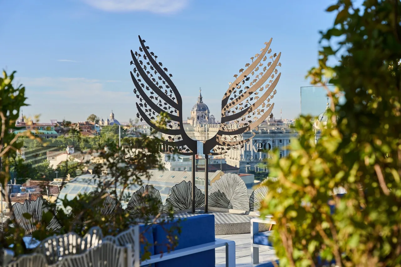 A winged metal sculpture on a rooftop terrace with Madrid rooftops and a domed building behind it