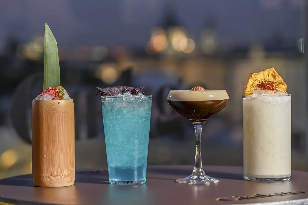 Four cocktails in different glasses on a bar with blurred city lights behind