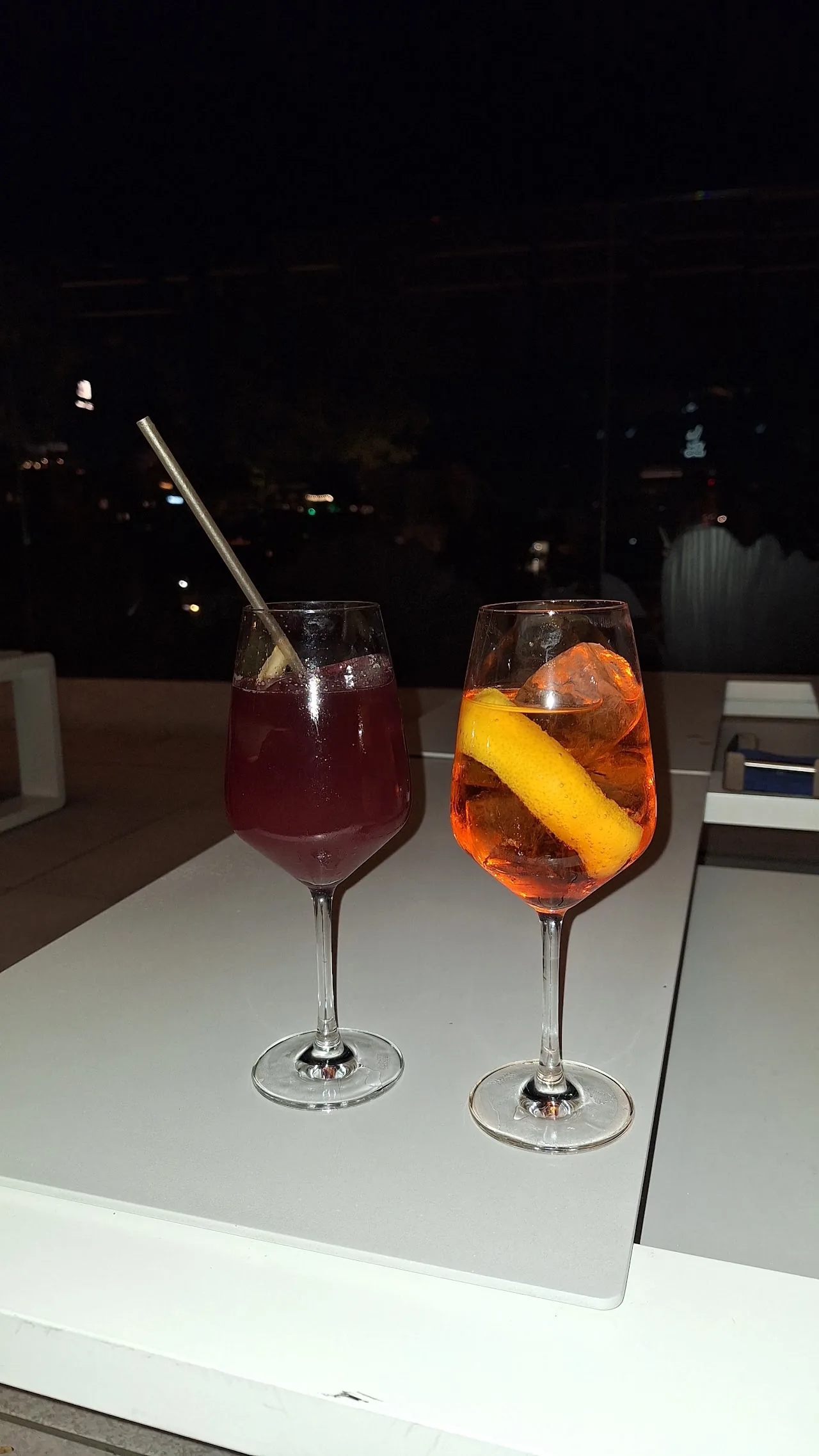 Two cocktails, one red and one orange, on a rooftop table