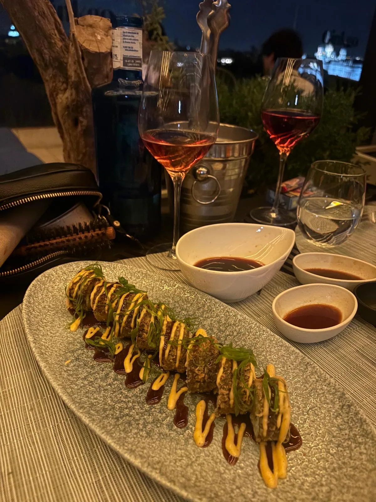 A sushi roll platter drizzled with sauce, served with soy dipping bowls