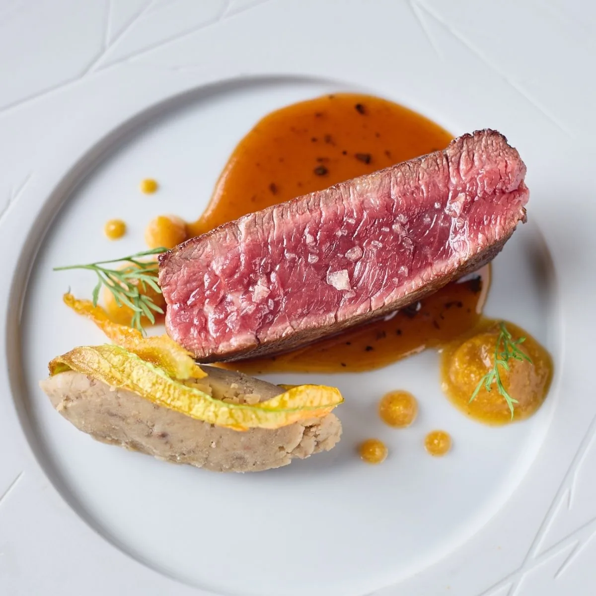 A slice of rare beef with foie gras and orange sauce on a white plate