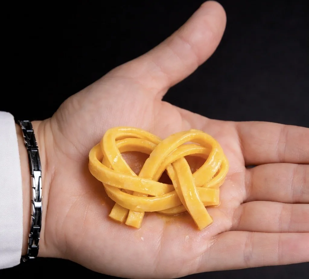 A hand holding a twisted nest of fresh golden pasta against a black background