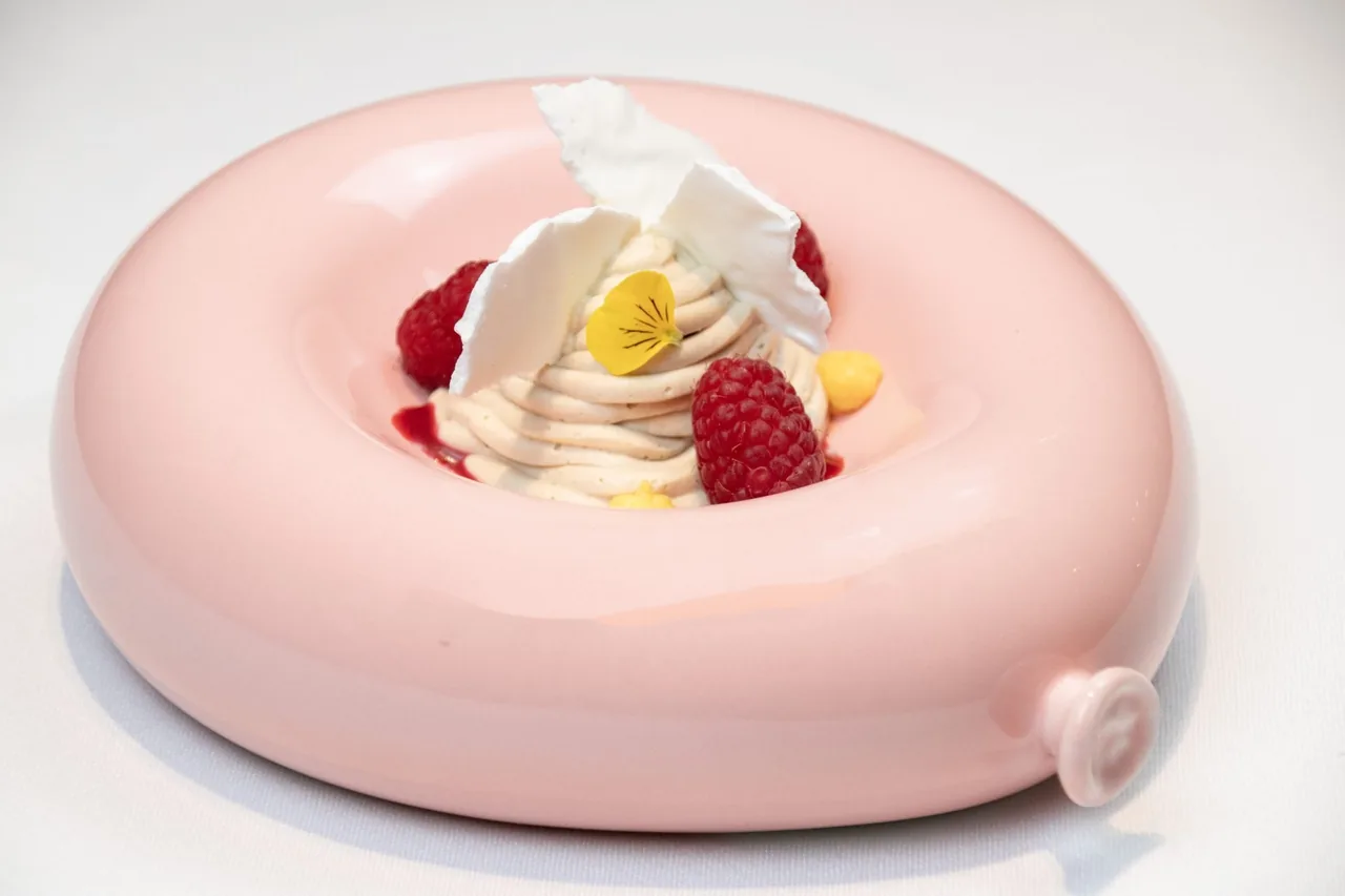 A pink ring-shaped dessert with cream, raspberries and a white crisp on top