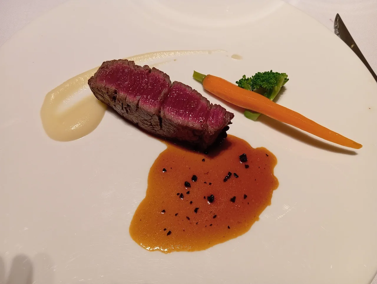 A slice of rare meat with a carrot and a dark sauce on a white plate