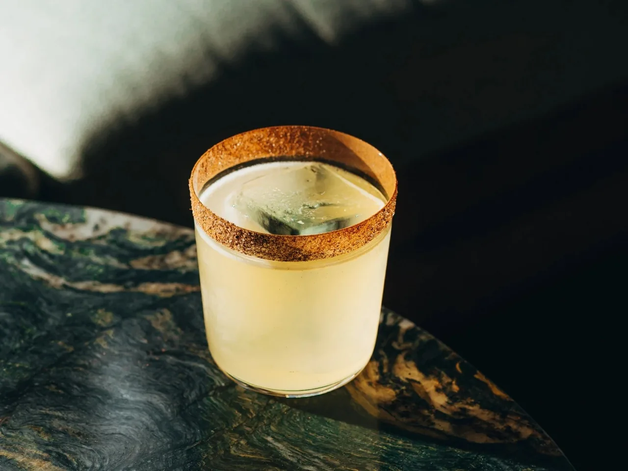 A cocktail in a rocks glass with a cork-coloured rim on a dark marble table