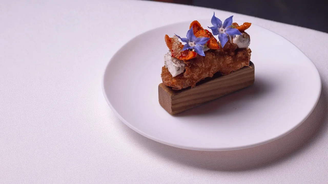 A rectangular layered dessert topped with orange flowers on a round white plate