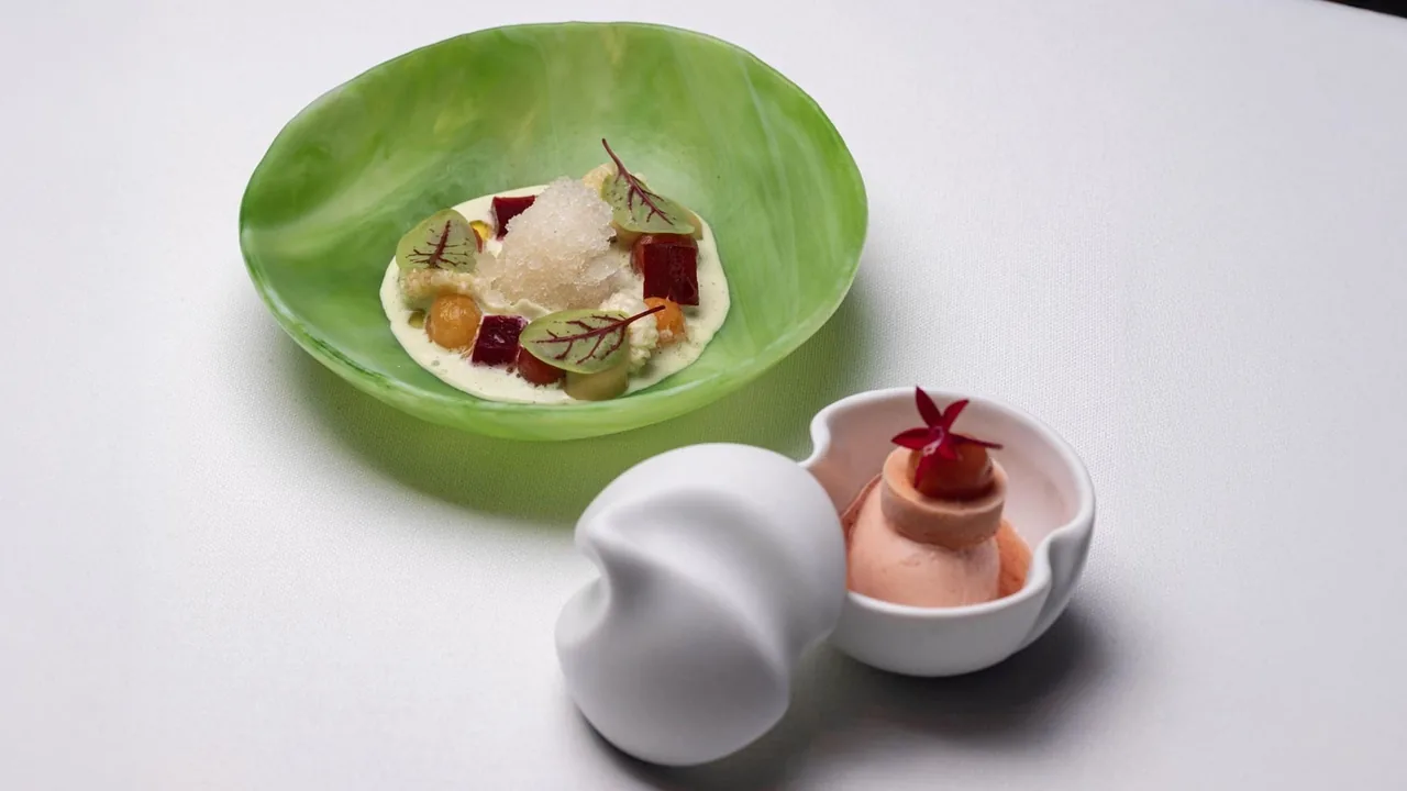 A green bowl of creamy dishes with a pink sphere and a small white bowl beside it