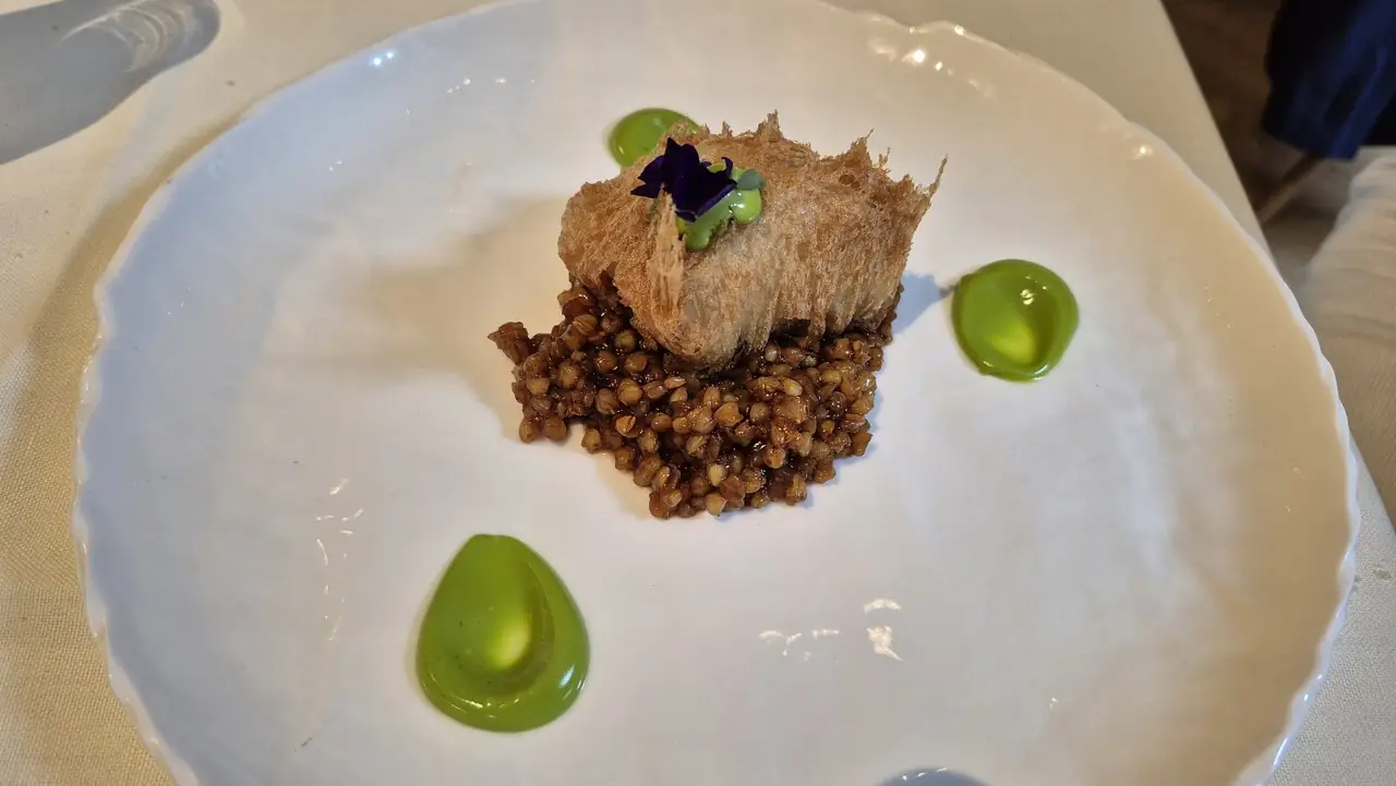 Crispy-skinned fish over grain with green sauce dots and an edible flower garnish
